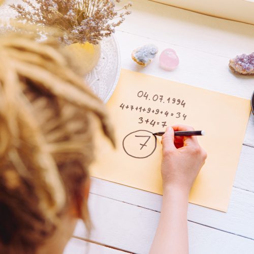 Above view of girl calculate Life path number on paper in home. Spiritual numerology concept.